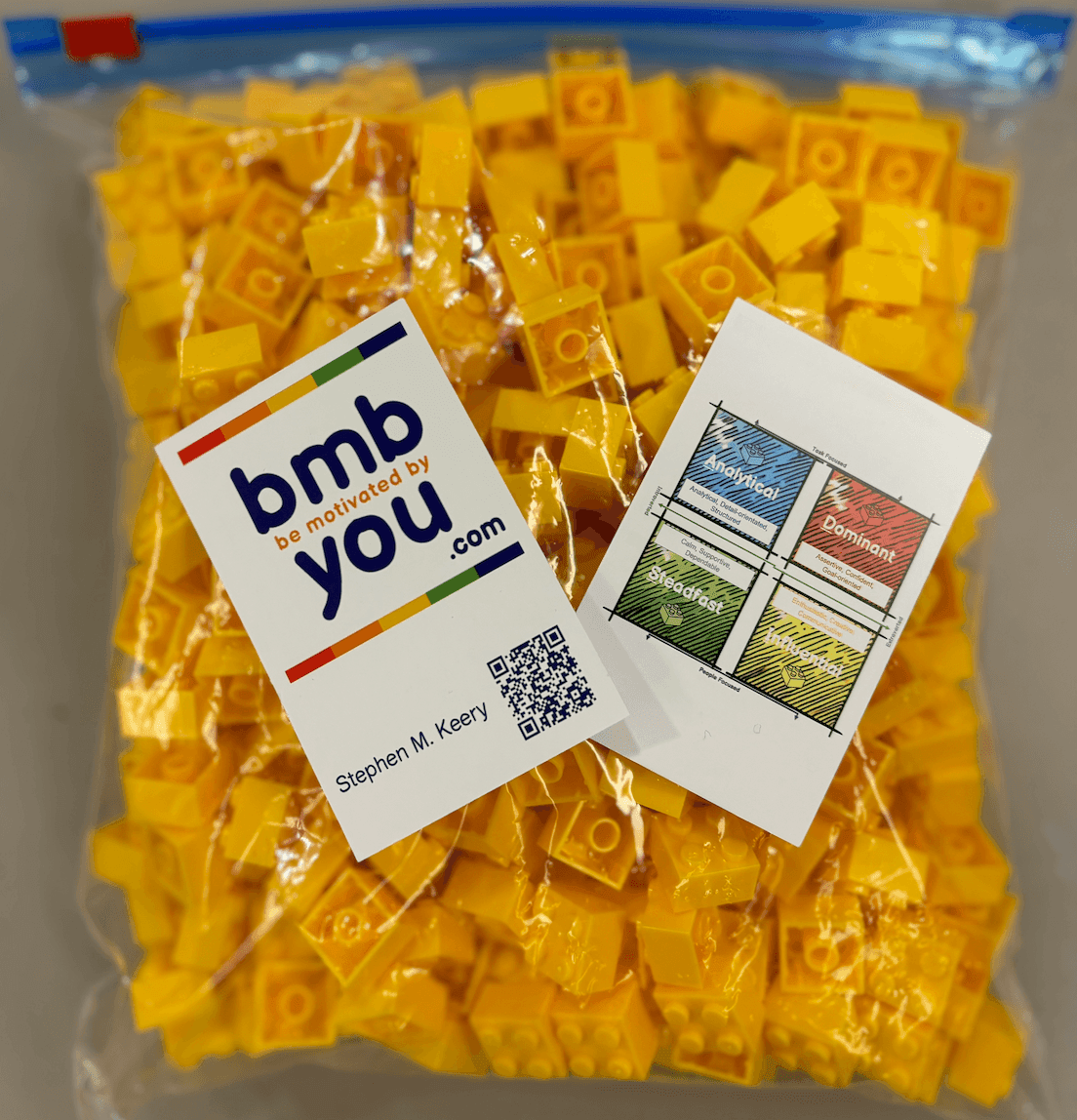 Bag of yellow plastic building blocks with business cards on top.